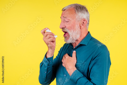 Senior man using an asthma inhaler in studio yellow background © yurakrasil