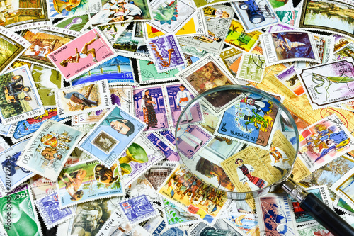 Background with a pile of colored stamps showing various activities and magnifying glass over them