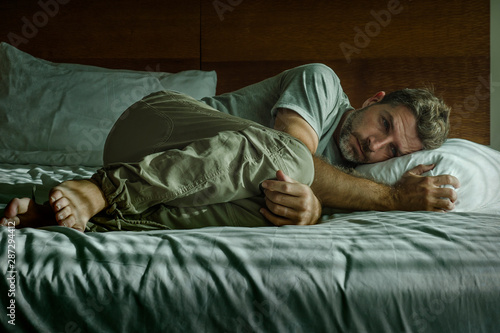 young attractive sad and depressed man crying helpless on bed at home bedroom feeling overwhelmed and desperate suffering depression problem photo