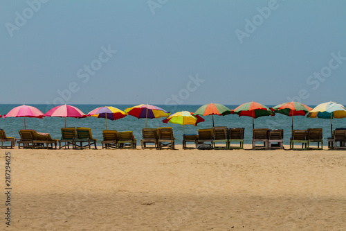 Row of covered wooden sun beds with colorful umbrellas on the beach in GOA  India. Sea summer background. Holiday template. Long shot.