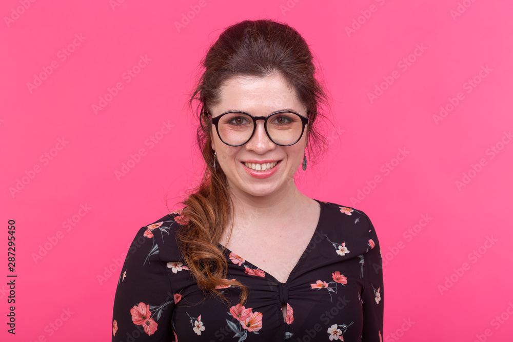 Portrait of a smart charming brown-eyed young positive woman in eyeglasses posing on a bright pink background Portrait of a smart charming brown-eyed young positive woman in eyeglasses posing on a bright pink background