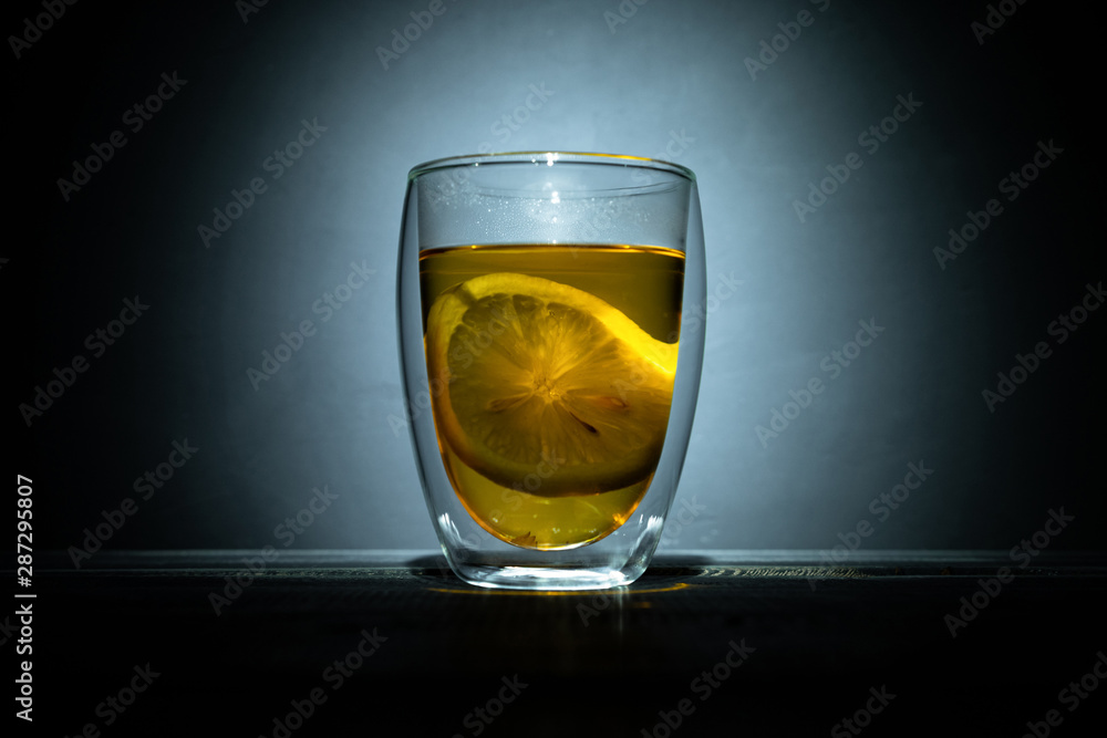 black tea with slice lemons in glass thermomug on dark background in spot light
