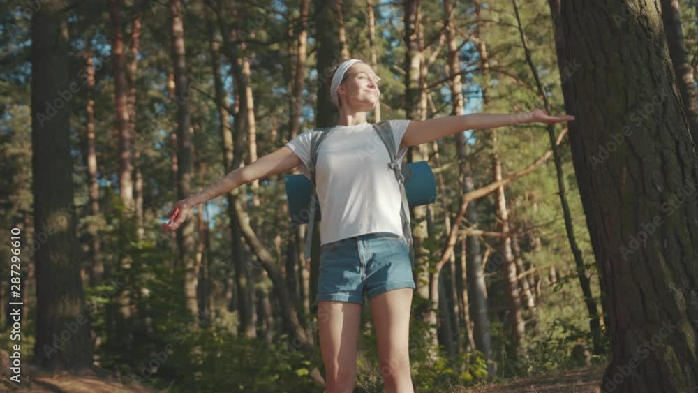 Charming attractive young woman stand smile look around in forest outdoors with backpack hiker camping hiking travel wood hike active journey vacation portrait slow motion Charming attractive young woman stand smile look around in forest outdoors with backpack hiker camping hiking travel wood hike active journey vacation portrait slow motion