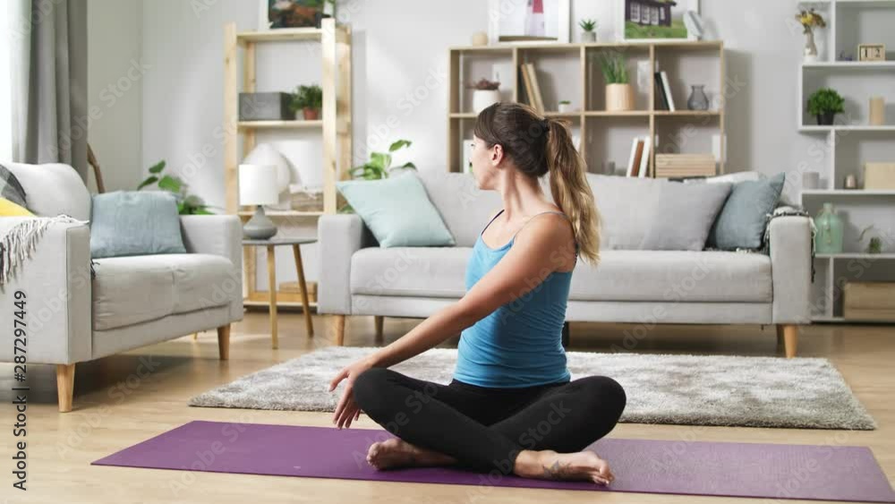 Relaxing young woman in sportswear sitting on floor in home and stretching spine Relaxing young woman in sportswear sitting on floor in home and stretching spine