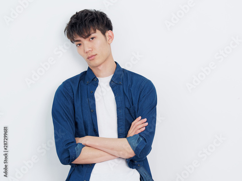 Fotografía Portrait of a handsome Chinese young man in blue shirt looking at camera with two arms crossed, serious expression, isolated on white background