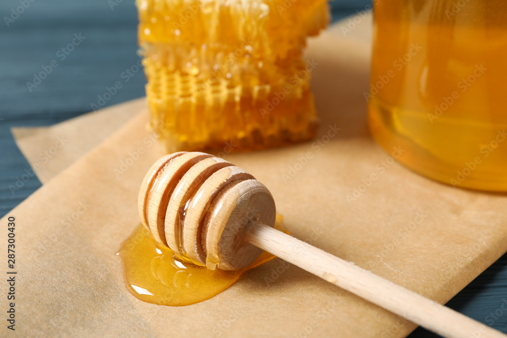 Glass jar with honey, dipper, honeycombs and parchment on wooden background, close up Glass jar with honey, dipper, honeycombs and parchment on wooden background, close up
