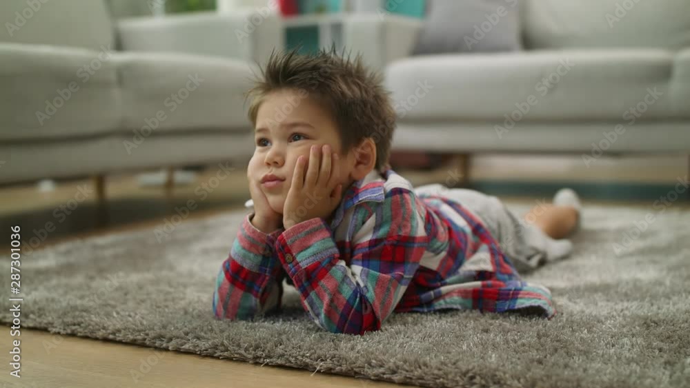 Boy carefully watches cartoons on TV lying on the floor in living room Boy carefully watches cartoons on TV lying on the floor in living room