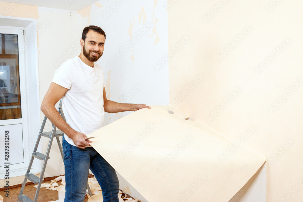 Man in with a scraper in the process of removing old wallpaper.