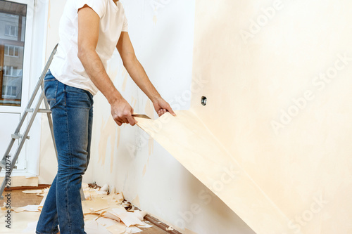 Man in with a scraper in the process of removing old wallpaper.