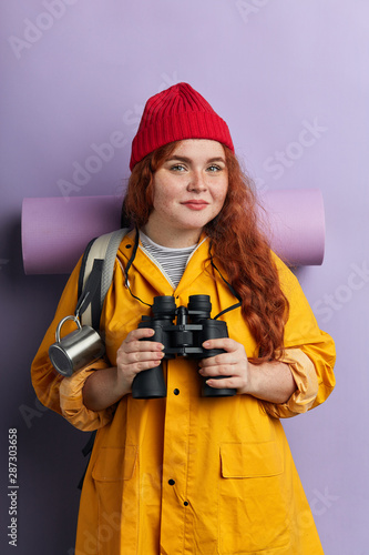 pleasant good looking woman in stylish clothes holding her binoculars and posing to the camera. close up portrait, isolated blue background studio shot