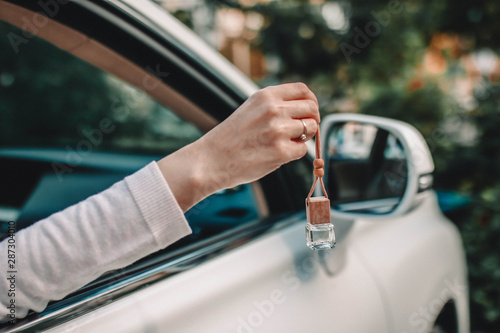 Small glass bottle with car perfume in female hand. Small glass bottle with car perfume hanging near the car.