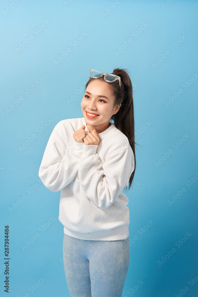 Happy woman keeps hands under chin looks joyfully at camera, notices something very pleasant, isolated over light blue background Happy woman keeps hands under chin looks joyfully at camera, notices something very pleasant, isolated over light blue background