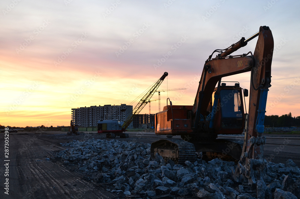 Large tracked excavator with hydraulic shears on a construction site against the background of the awesome sunset. Road repair, asphalt replacement. Small roughness sharpness, possible granularity Large tracked excavator with hydraulic shears on a construction site against the background of the awesome sunset. Road repair, asphalt replacement. Small roughness sharpness, possible granularity