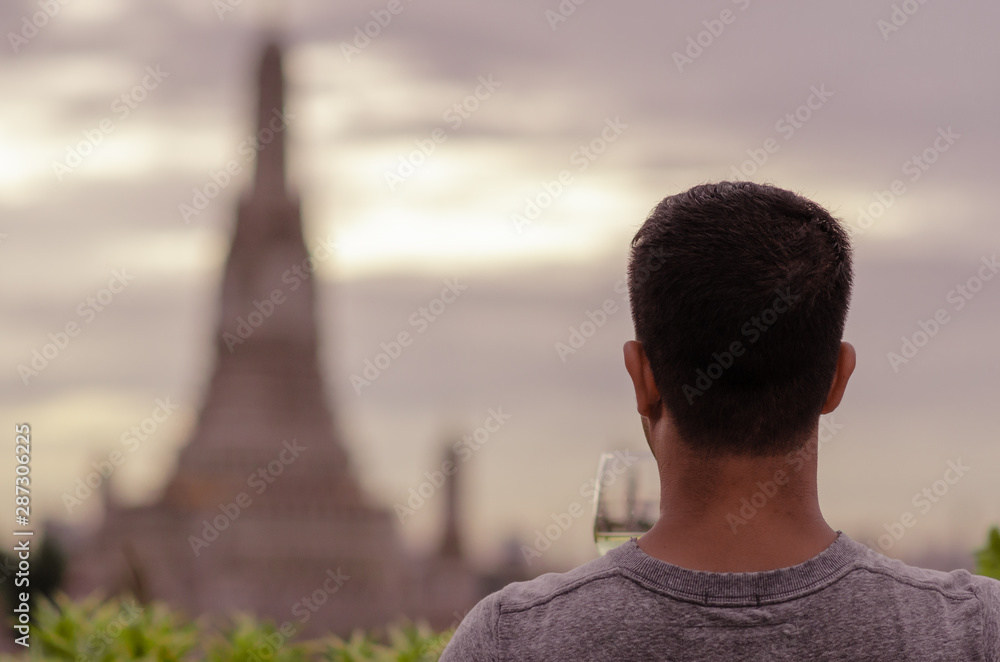 A tourist holding a glass of white wine looking at blurred background of temple.