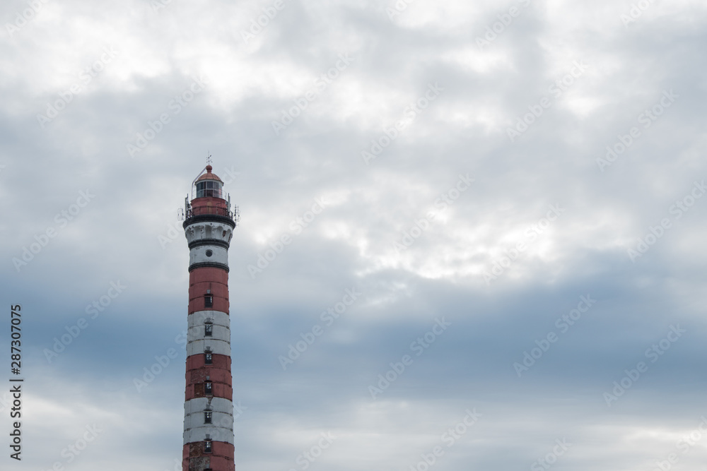 Colorful lighthouse against the sky. An old tower with a lantern, for sending light signals to ships, boats, yachts, sailboats, water transport. Designed for orientation, warns of danger. Built on the