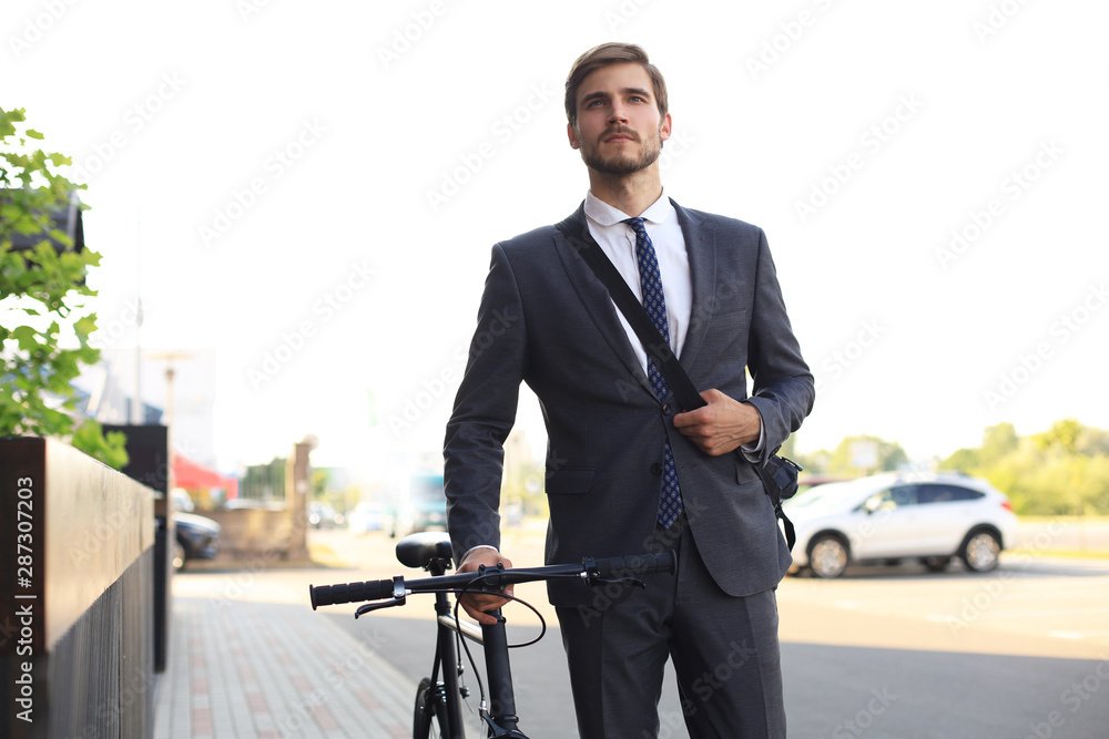 Pensive young businessman walking with bicycle on the street in city. Pensive young businessman walking with bicycle on the street in city.