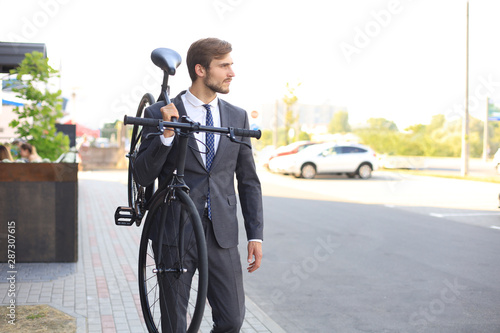 Handsome young businessman carrying his bicycle on shoulder while walking outdoors.