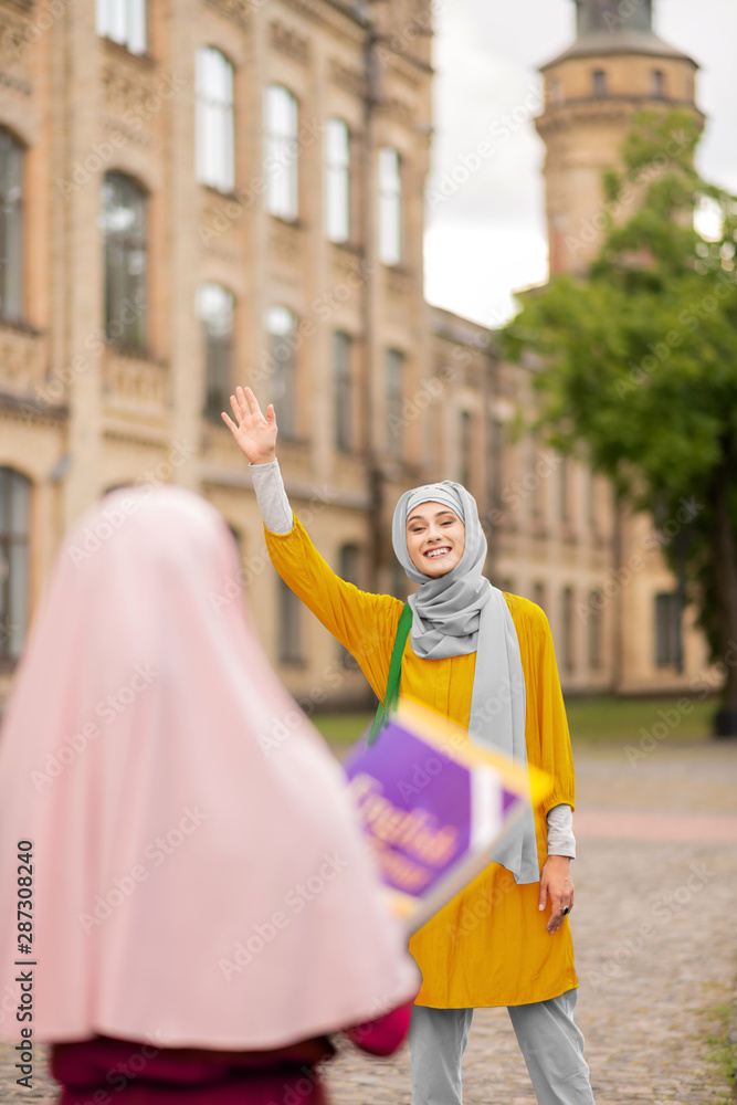 Muslim student waving her friend while meeting near university