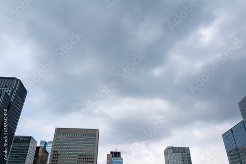 都会の高層ビルと灰色の雲が広がる曇り空