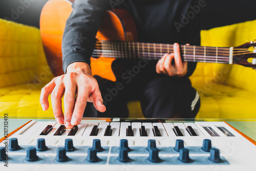 male songwriter playing guitar and keyboard for creating melody, harmony in a song. song writing concept