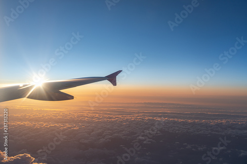 Up in the air, view of aircraft wing silhouette with dark blue sky horizon and cloud background in sun rise time, viewed from airplane window