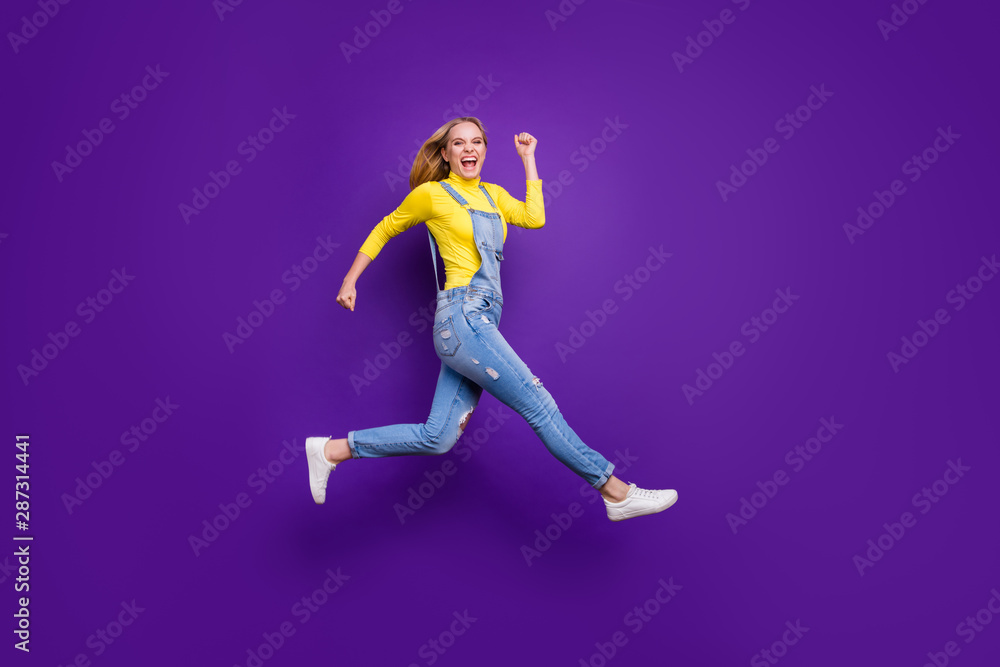 Full length photo of cheerful teenager running screaming wearing yellow turtleneck denim jeans overalls isolated over violet purple background