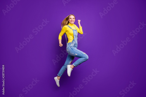 Full size photo of cheerful girl raising her fists screaming yeah wearing yellow turtleneck denim jeans isolated over purple violet background