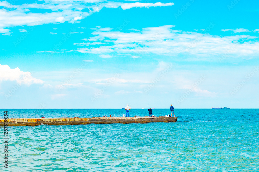 Fishermen on the pier with a fishing rods. Fishermen on the background of the horizon. Seascape from the pier.