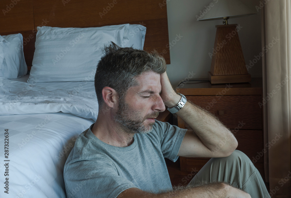 young depressed and desperate man sitting on bedroom floor next to bed suffering depression and anxiety feeling overwhelmed and helpless young depressed and desperate man sitting on bedroom floor next to bed suffering depression and anxiety feeling overwhelmed and helpless