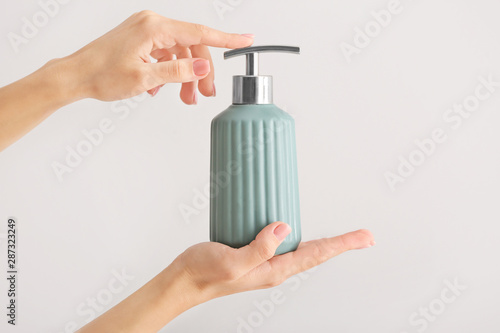 Female hands with soap in bottle on light background