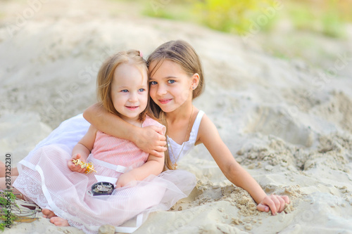 two little girls play outdoors, sisters play in the sand, hug and smile