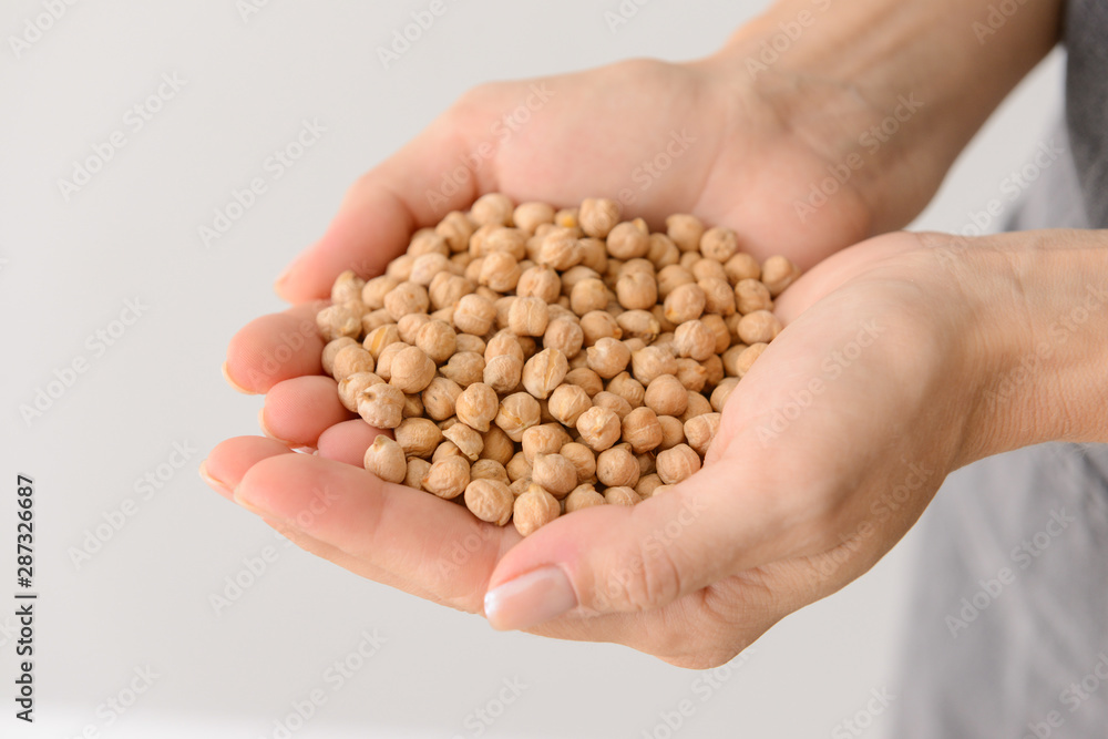 Woman holding raw chickpea on light background, closeup