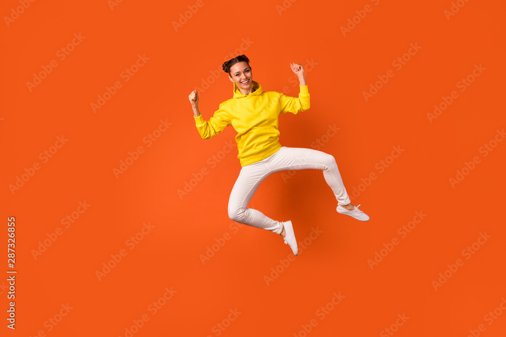 Full size photo of cheerful millennial jumping with raised hands arms wearing pants trousers isolated over orange background