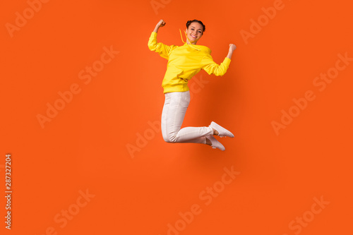 Full body photo of lovely teen raising fists smiling isolated over orange background