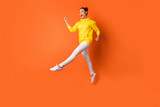 Full size photo of cute childish person moving raising legs wearing white pants trousers isolated over orange background