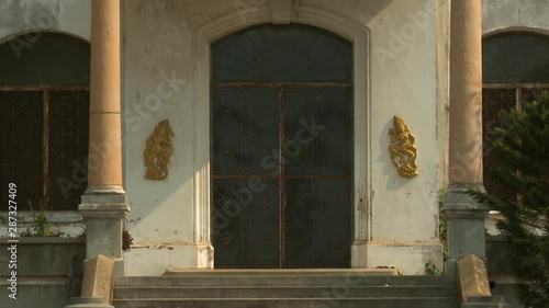 A daylight front view of a Buddhist building showing its double glass doors with transom and with matching glass windows secured with metal grill works while a Buddha appliqu� decorates both sides
