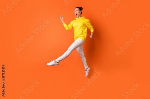 Full size photo of cute childish person moving raising legs wearing white pants trousers isolated over orange background