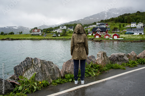 A girl in a jacket looks at a town. Explore Norway. Beautiful landscape in North. Ocean and mountain. Architecture, scandinavian style. Enjoy the moment, relaxation. Travel, adventure, lifestyle