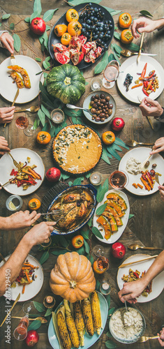 Thanksgiving, Friendsgiving holiday celebration. Flat-lay of friends feasting at Thanksgiving Day table with turkey, pumpkin pie, roasted vegetables, fruit, rose wine, top view, narrow composition
