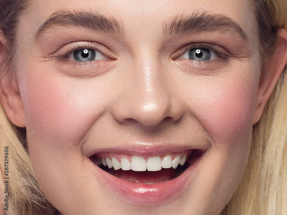 Closeup of beautiful young woman's face with clean perfect skin and hair smiling at camera. Portrait of a blonde with blue eyes. Spa, skin care and wellness. Isolated on white background Closeup of beautiful young woman's face with clean perfect skin and hair smiling at camera. Portrait of a blonde with blue eyes. Spa, skin care and wellness. Isolated on white background