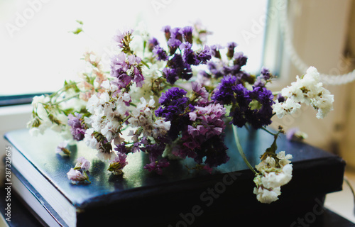 A bouquet of dried violet, pink and white wildflowers lying on the book. Bright flowers lit by sunlight. Soft selective focus, macro flowers. Photo background