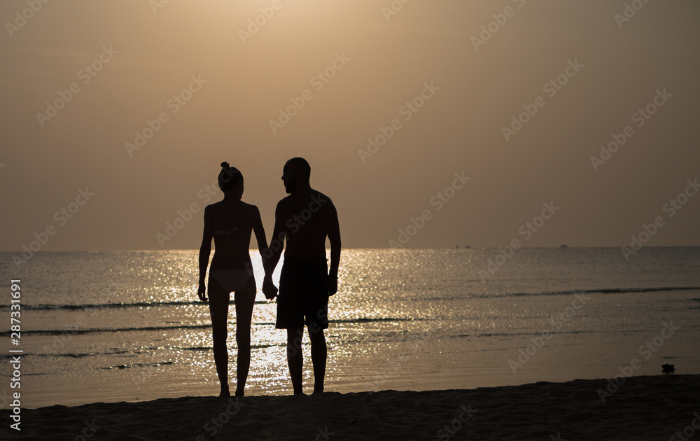 Silhouette of a man and a woman holding hands on the beach in sunset
