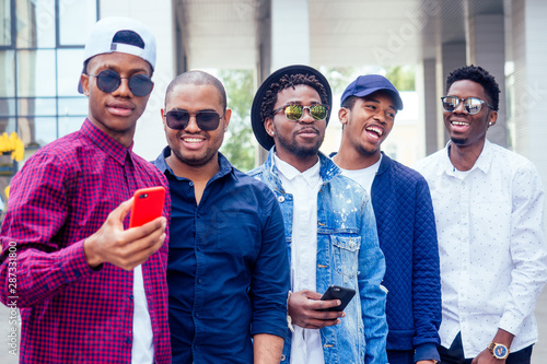a group of five fashionable cool African American guys students communicating on the street looking at smartphone take pictures selfie on phone in street photo