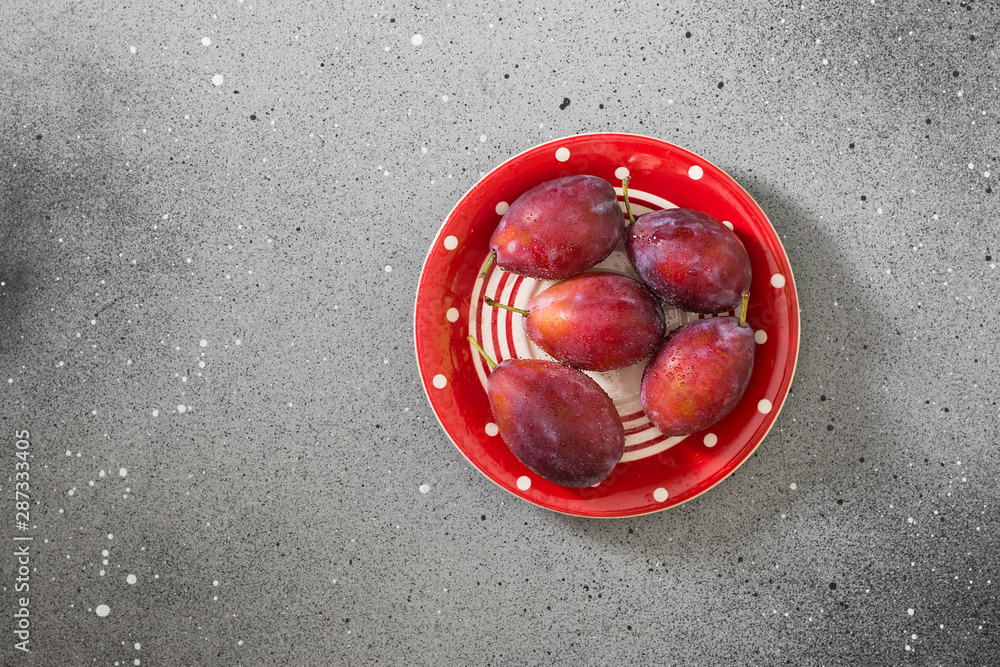 Plums in a red plate on a gray table. Autumn harvest