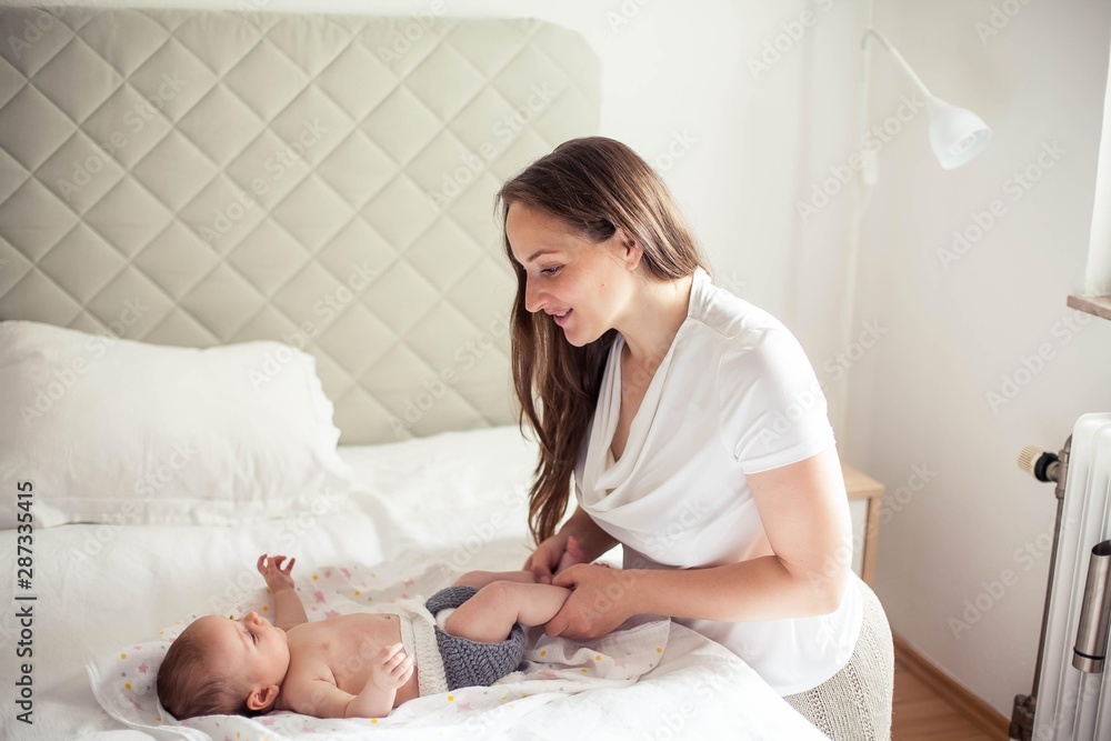 Young beautiful mother holds a baby. Mom gives the baby a massage on the bed. Young beautiful mother holds a baby. Mom gives the baby a massage on the bed.