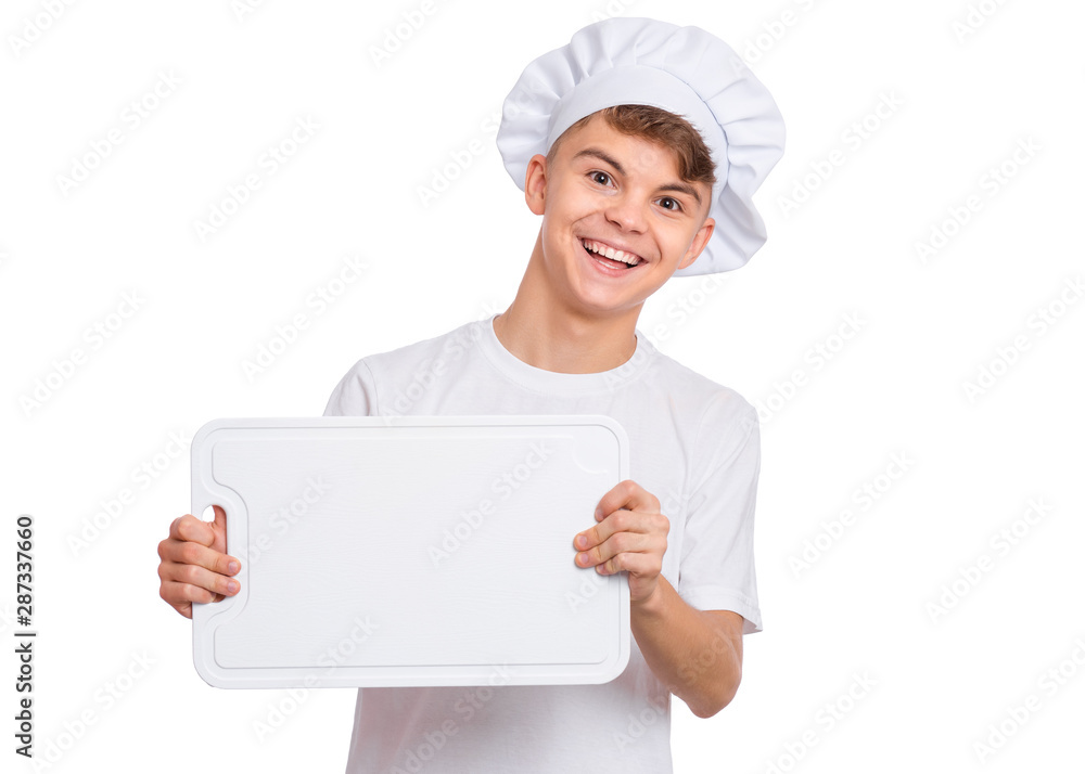 Happy handsome teen boy in chef hat holding cutting board, isolated on white background. Portrait of cute smiling child showing cutting board with space for text. Tools and equipment for cooking. Happy handsome teen boy in chef hat holding cutting board, isolated on white background. Portrait of cute smiling child showing cutting board with space for text. Tools and equipment for cooking.