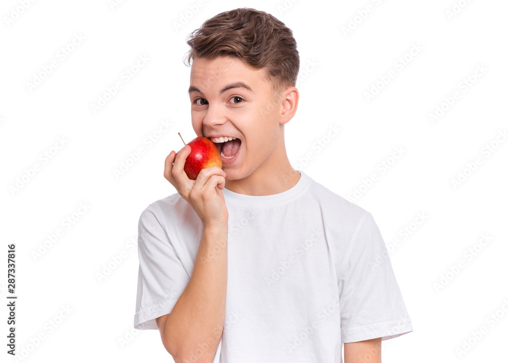 Smiling handsome young teen boy holding and eats fresh red apple, isolated on white background. Portrait of cute happy child bites apple. Delicious vegetables, organic natural healthy food produce. Smiling handsome young teen boy holding and eats fresh red apple, isolated on white background. Portrait of cute happy child bites apple. Delicious vegetables, organic natural healthy food produce.