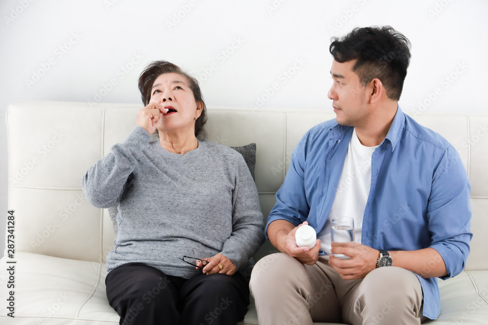 Asian senior woman mother with young man son with medicine and grass of water in living room Asian senior woman mother with young man son with medicine and grass of water in living room