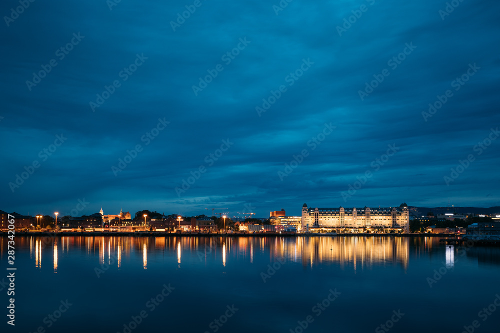 Oslo, Norway. Night View Embankment And Residential Multi-storey House On Langkaia Street In City Center In Oslo, Norway. Summer Evening. Residential Area Reflected In Sea Waters
