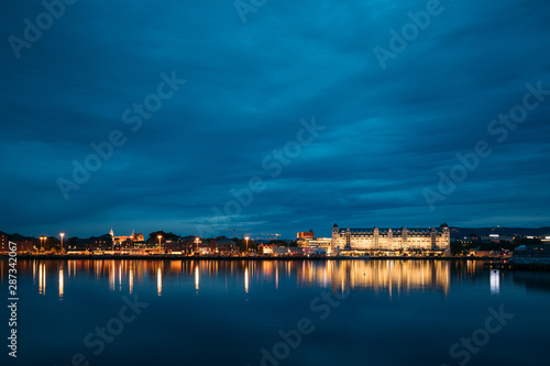 Oslo, Norway. Night View Embankment And Residential Multi-storey House On Langkaia Street In City Center In Oslo, Norway. Summer Evening. Residential Area Reflected In Sea Waters